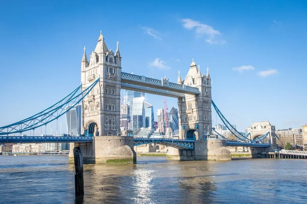 An editorial-style image showcasing the iconic Tower Bridge over the River Thames in London, with modern skyscrapers visible through its arches. The image is well-composed, brightly lit, and sharp, capturing the details of the bridge and the surrounding urban environment.