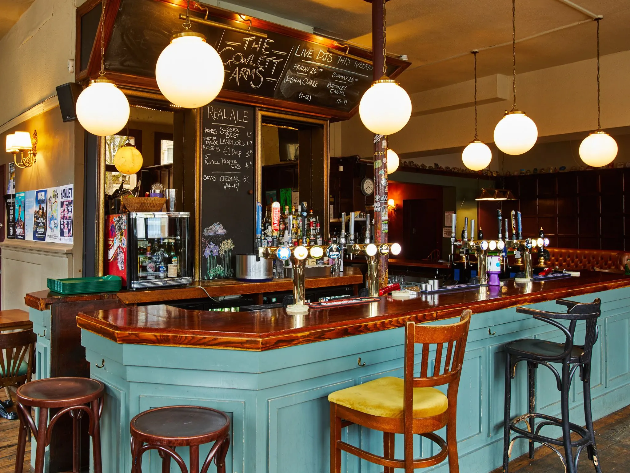 A well-composed and sharp photograph showcasing the interior of a traditional pub bar. The lighting is even, illuminating the various details from the polished wooden countertop and painted bar front to the numerous beer taps and the handwritten chalkboard menu. The colors are natural and accurate, contributing to a highly photo-realistic appearance. All key elements, including the bar, taps, and chalkboard, are in clear focus.