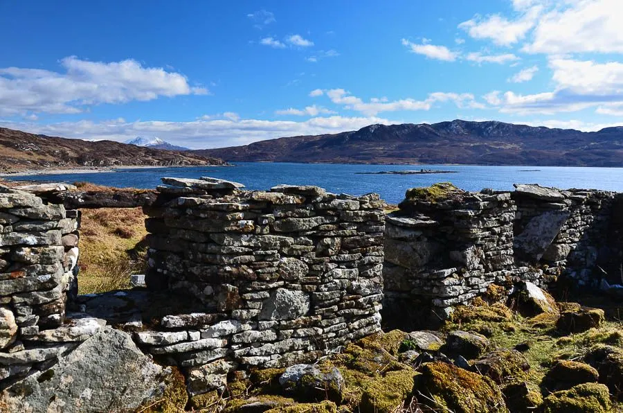 The image is well-lit with vibrant and color-accurate representation of a sunny day. Both the foreground stone structure and the background lake and mountains are sharp and in focus, contributing to its strong photo-realism. The composition effectively uses the foreground element to frame the distant landscape, although it occupies a significant portion of the frame.