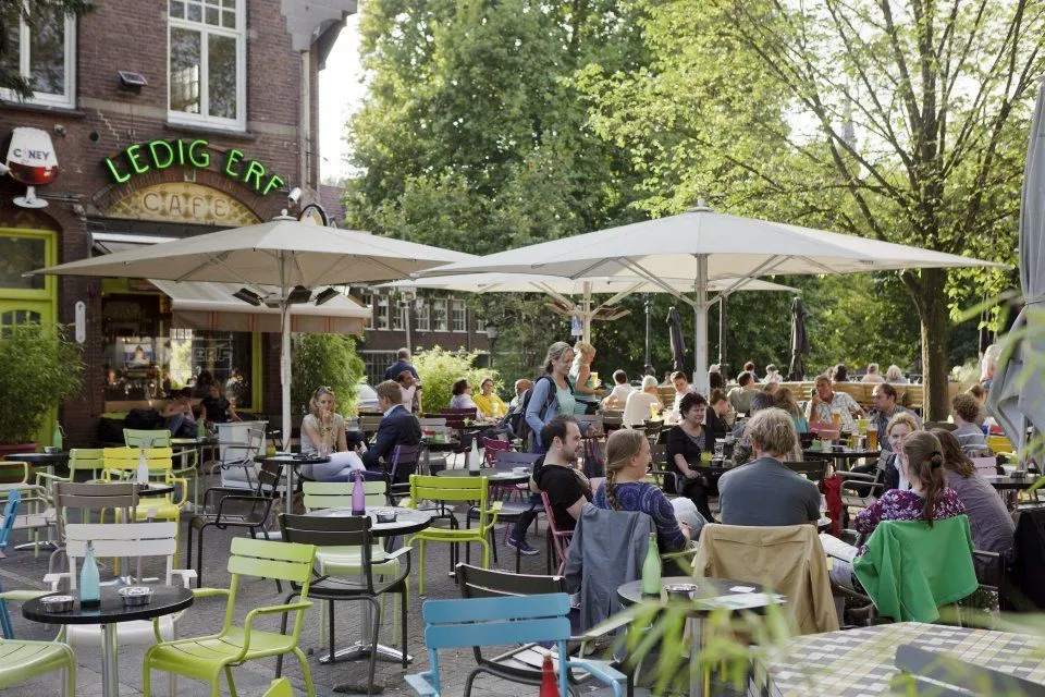 This image captures a vibrant outdoor cafe scene, well-lit by natural daylight. The colors are accurate and the photo is highly realistic, presenting a lively atmosphere. The composition is effective in conveying the busy cafe setting, though it's quite packed with elements. Most key subjects are in focus, contributing to a clear and engaging view.