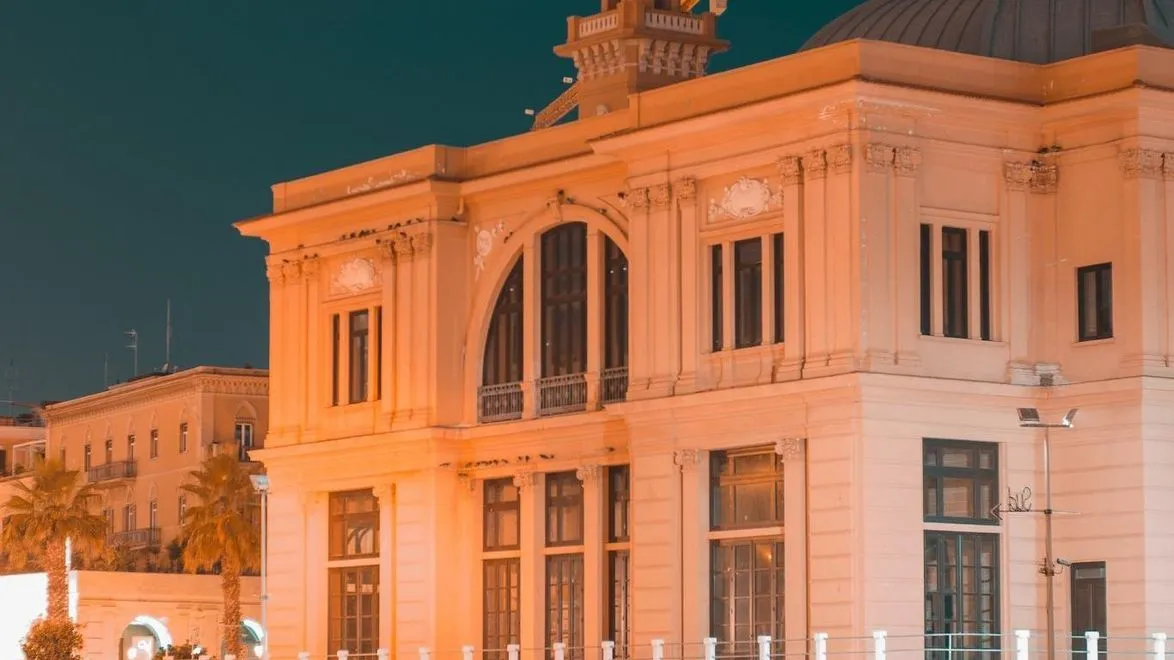 The image captures a detailed close-up of an ornate building facade, likely at dusk or night, illuminated by warm artificial light set against a deep blue sky.