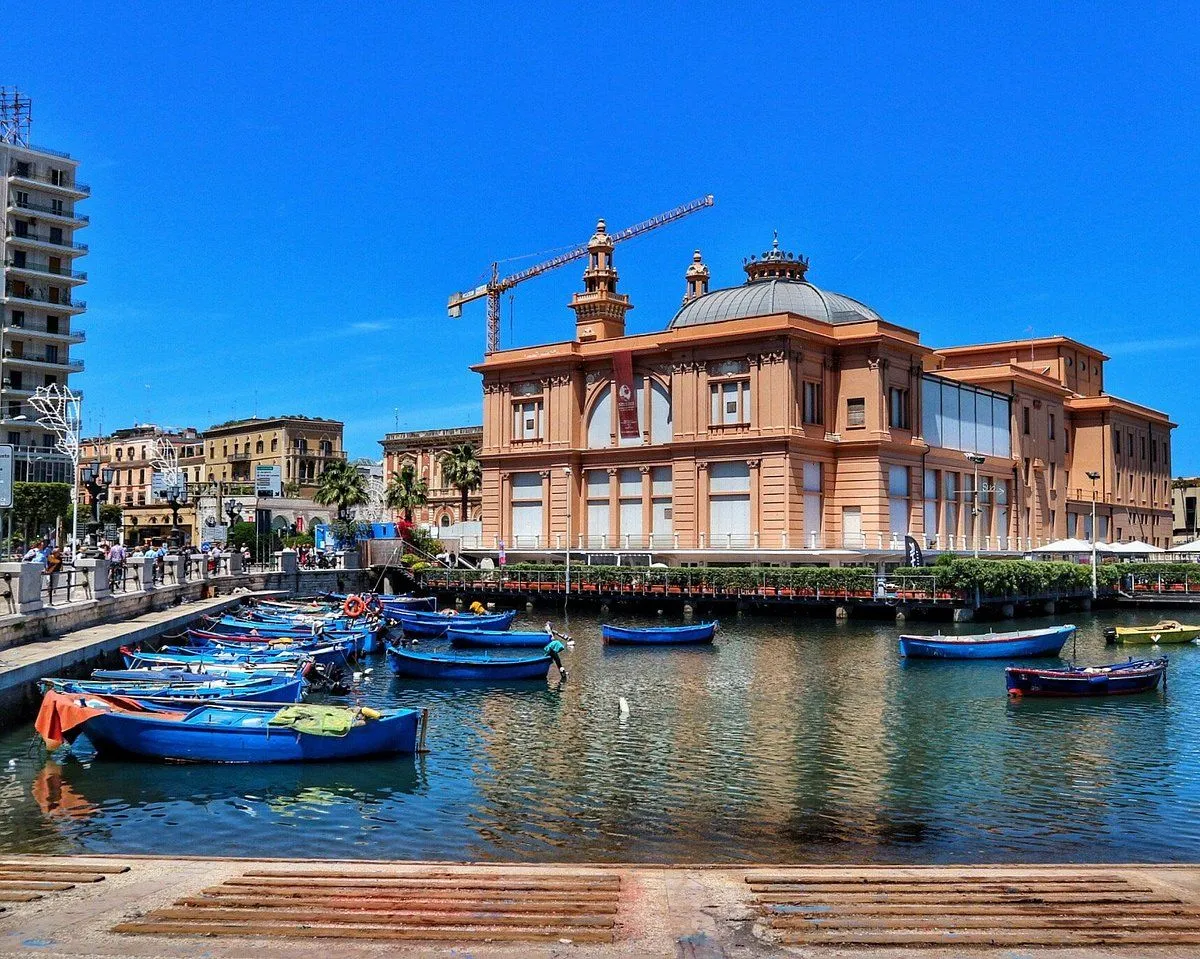 A vibrant editorial-style image showcasing a grand historic building with a domed roof and a construction crane, situated by a harbor filled with numerous blue fishing boats under a bright, clear blue sky.
