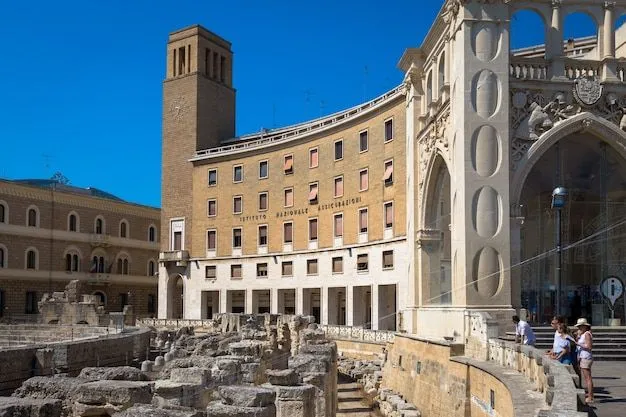 A vibrant outdoor shot showcasing a historical urban landscape featuring a modern-era curved building with a prominent tower, an adjacent ornate stone structure, and ancient ruins in the foreground under a clear blue sky.