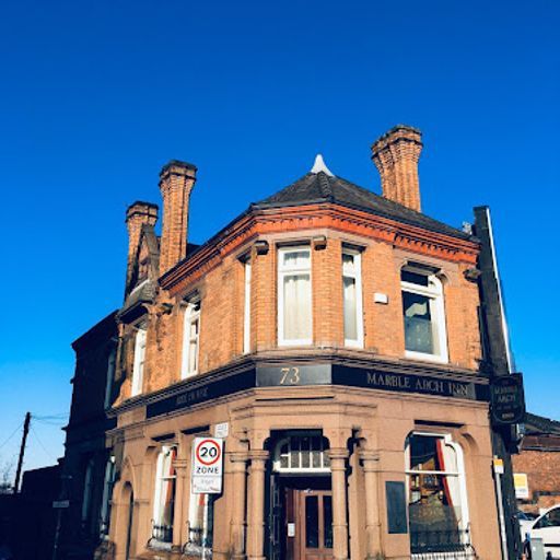 The image is well-composed, showcasing the building's facade from a slightly angled perspective. The lighting is excellent, with natural sunlight illuminating the brickwork and creating a warm ambiance. The image is sharp, capturing details like the brick texture and the sign's lettering. The colors are accurate, with vibrant blues in the sky and warm tones in the brickwork. The image is photorealistic and captures the building's architectural features well. The key elements, including the sign and the building's facade, are in focus. Overall, the image meets the criteria for a high-quality exterior photograph. The only minor weakness is the presence of a street sign, which could be considered an unwanted element.