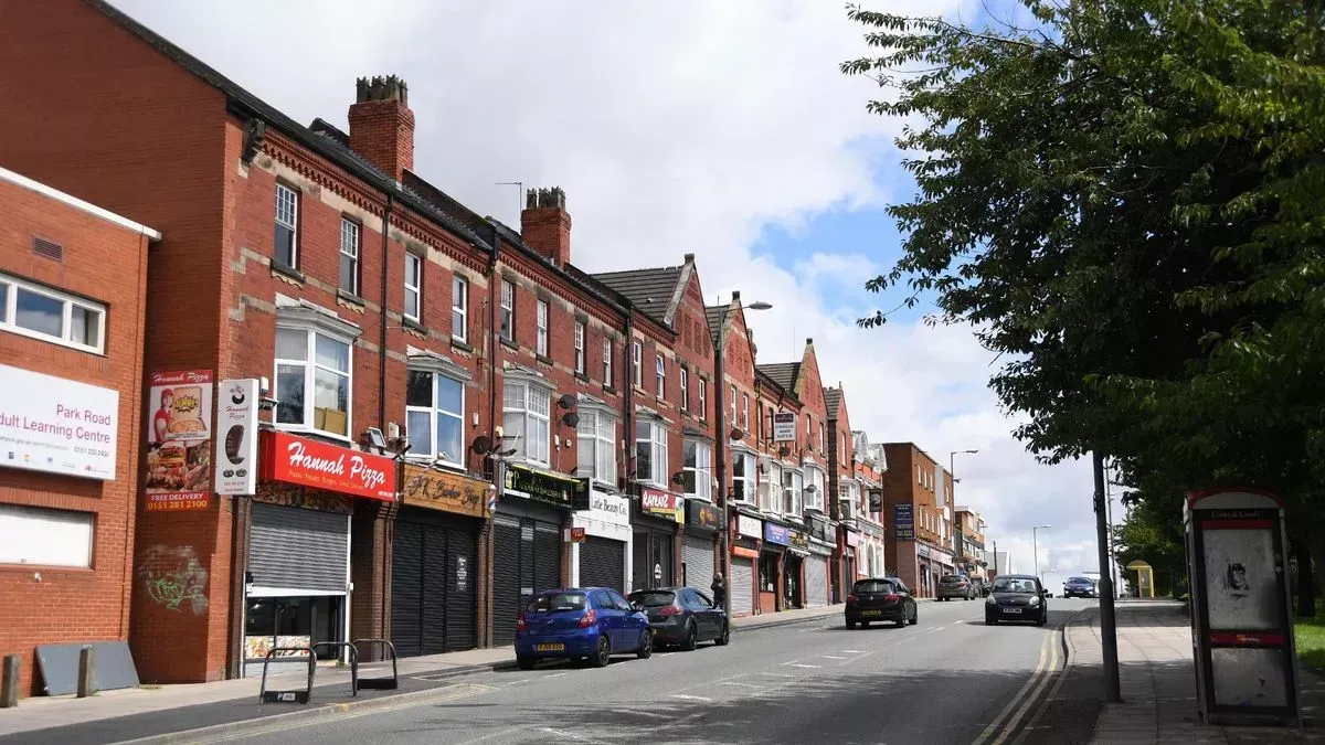An image depicting a row of traditional brick buildings housing various shops along a street, with parked cars and a road leading into the distance under a cloudy sky.