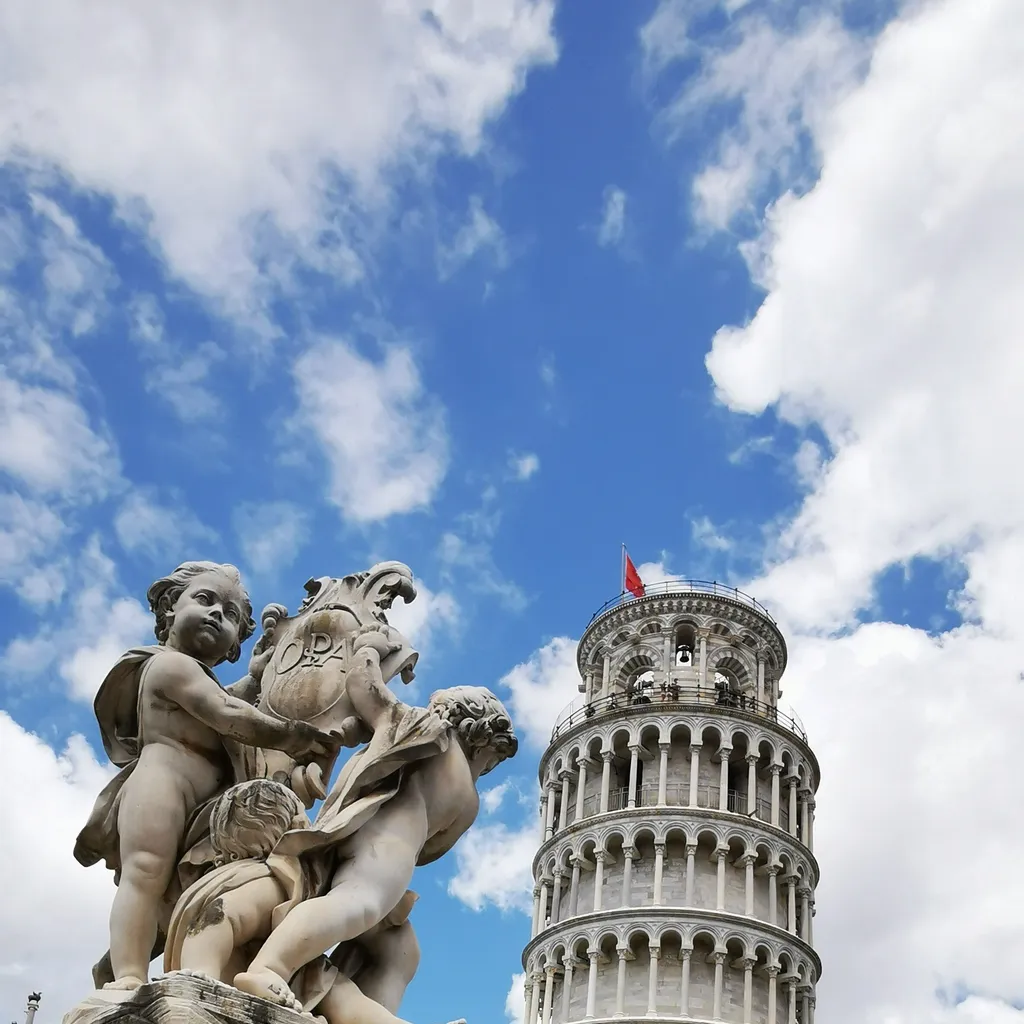 An editorial style image showcasing the Leaning Tower of Pisa in the background, framed by a classical marble sculpture featuring cherubs in the foreground. The sky is blue with scattered white clouds.