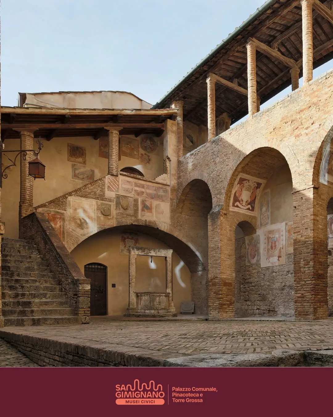 An outdoor shot of an ancient European courtyard featuring aged brick walls, multiple arches, stone stairs, and faded frescoes on the walls.
