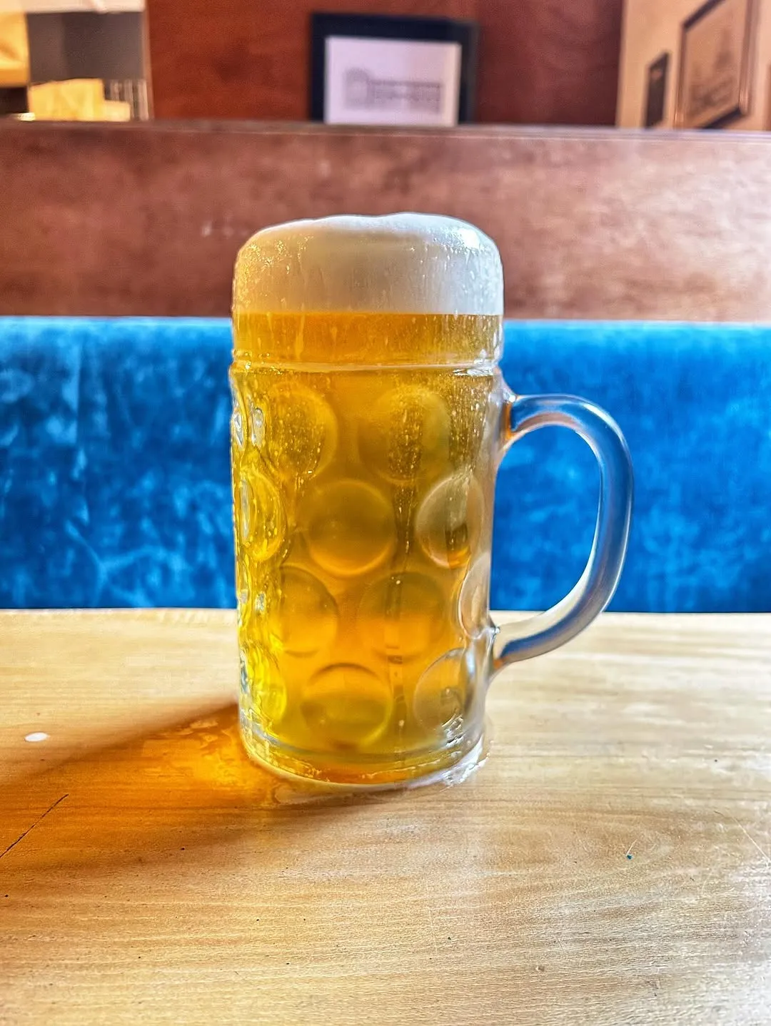 A well-composed and sharply focused image of a full beer mug with a generous head of foam. The lighting is excellent, showcasing the vibrant golden color of the beer and the crisp texture of the foam. The background is subtly blurred, enhancing the subject. The image appears photo-realistic and color-accurate, making the drink look appealing.