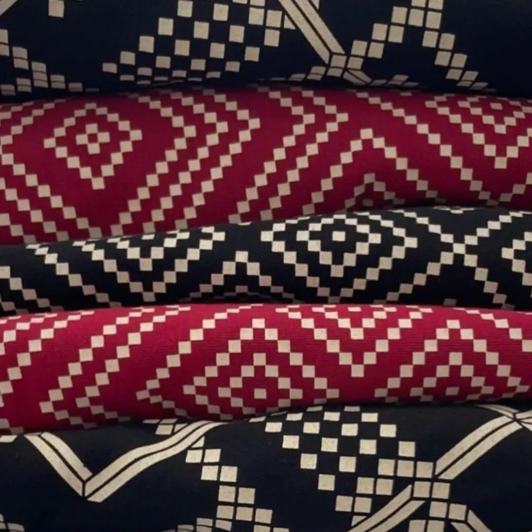 An image featuring a stack of folded fabrics with alternating black and red geometric patterns. The white squares of the pattern create a dynamic visual.