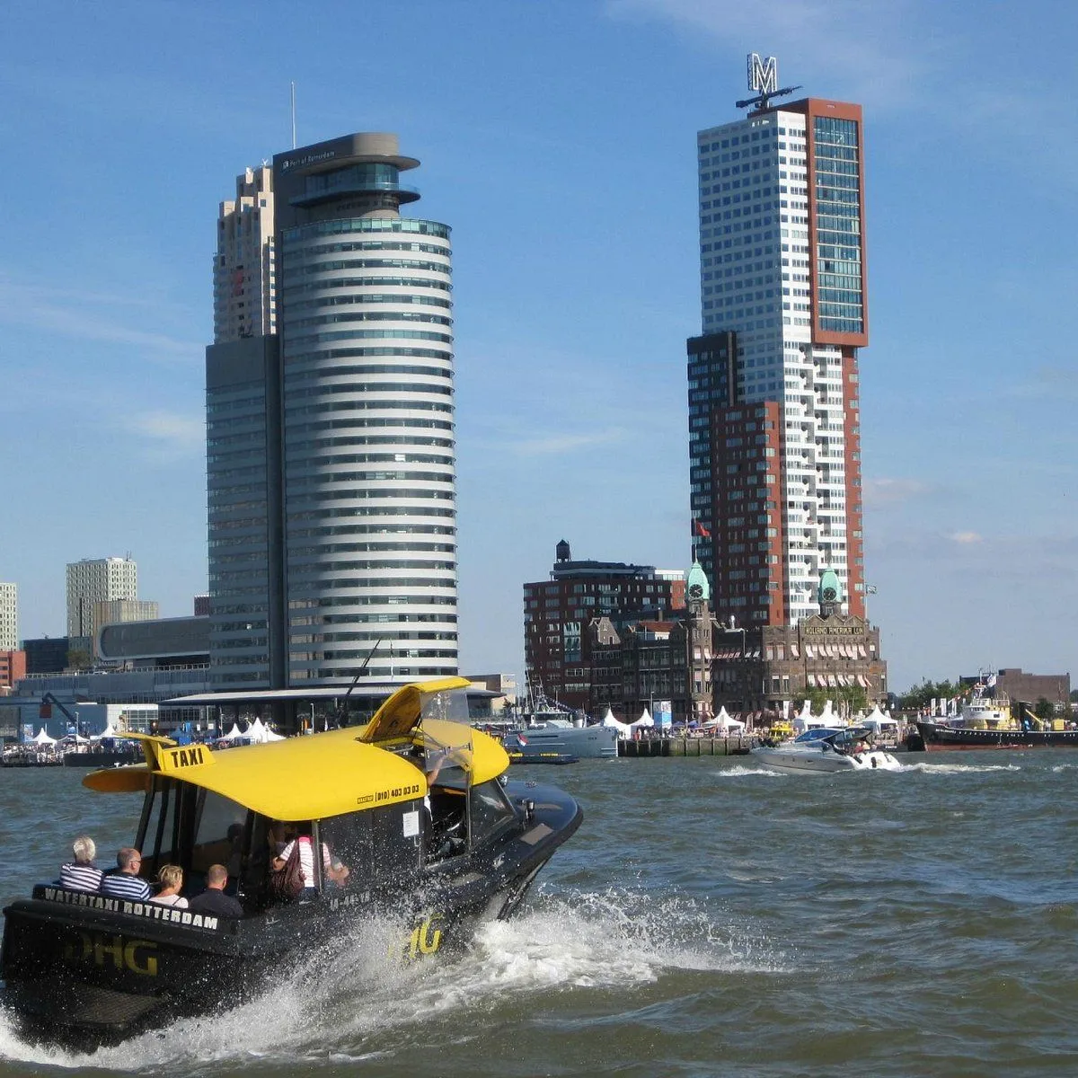 An editorial image showcasing a water taxi moving through a river with modern cityscape buildings in the background. The scene is well-lit and dynamic, capturing a clear day in an urban environment.