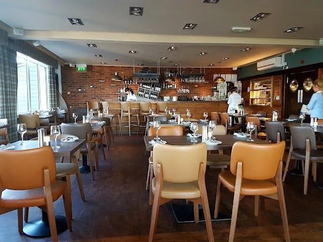 An editorial quality image showcasing the interior of a restaurant with set dining tables and a bar area.