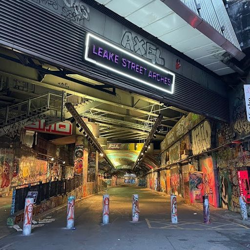 The image is an example of exterior photography. It shows a street scene with graffiti-covered walls and a colorful floor. The composition is well-centered, and the graffiti provides a visually appealing backdrop for the scene. The image is well-lit and appears to be taken during the day. It seems to be color-accurate with no apparent color cast or saturation issues. The sharpness is adequate but not exceptional; finer details are not as crisp as they could be in a high-quality photo. Based on the above criteria: - The image successfully communicates the essence of the space, with a slight deduction for the lack of sharpness. - There's some leniency given for exterior and interior photography. Score: 85 Strengths: - Good representation of the location's atmosphere - Adequate lighting and color accuracy - The photo tells a story of the location's history and culture Weaknesses: - Could be sharper in terms of detail capture