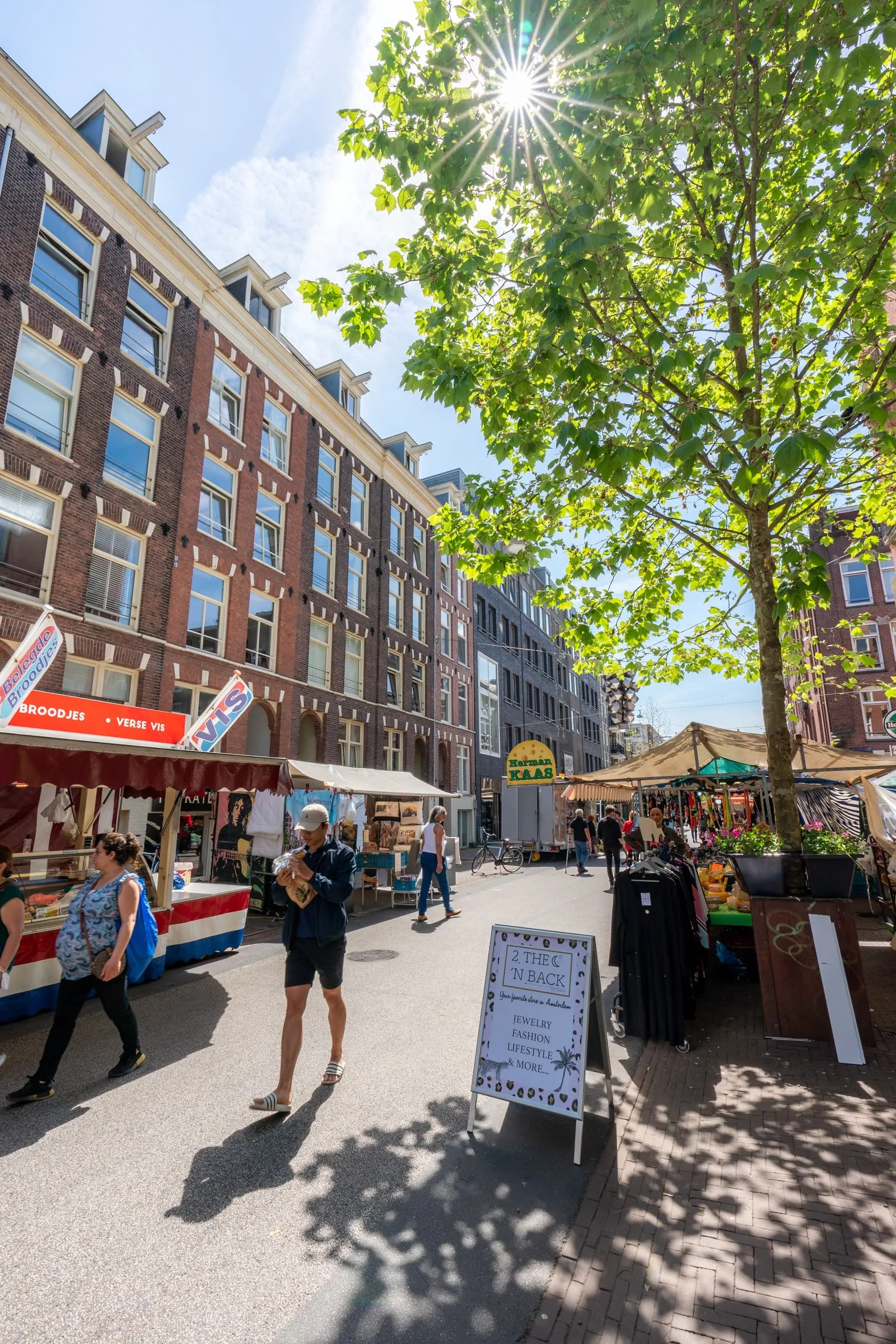 A vibrant and well-composed photo of a bustling street market, showcasing architectural details of buildings, market stalls, and people enjoying the day. The lighting is good, highlighting details and colors.