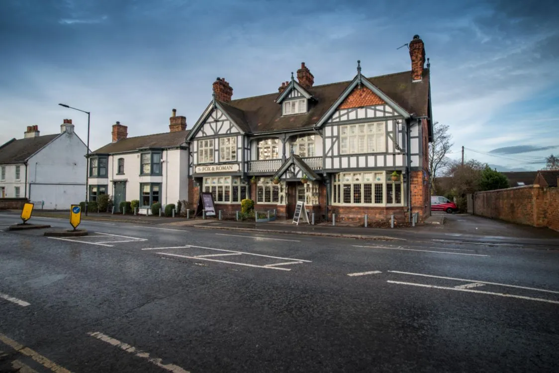 A well-composed and sharp exterior photograph of "The Fox & Roman" pub, showcasing its traditional architecture on an overcast day.