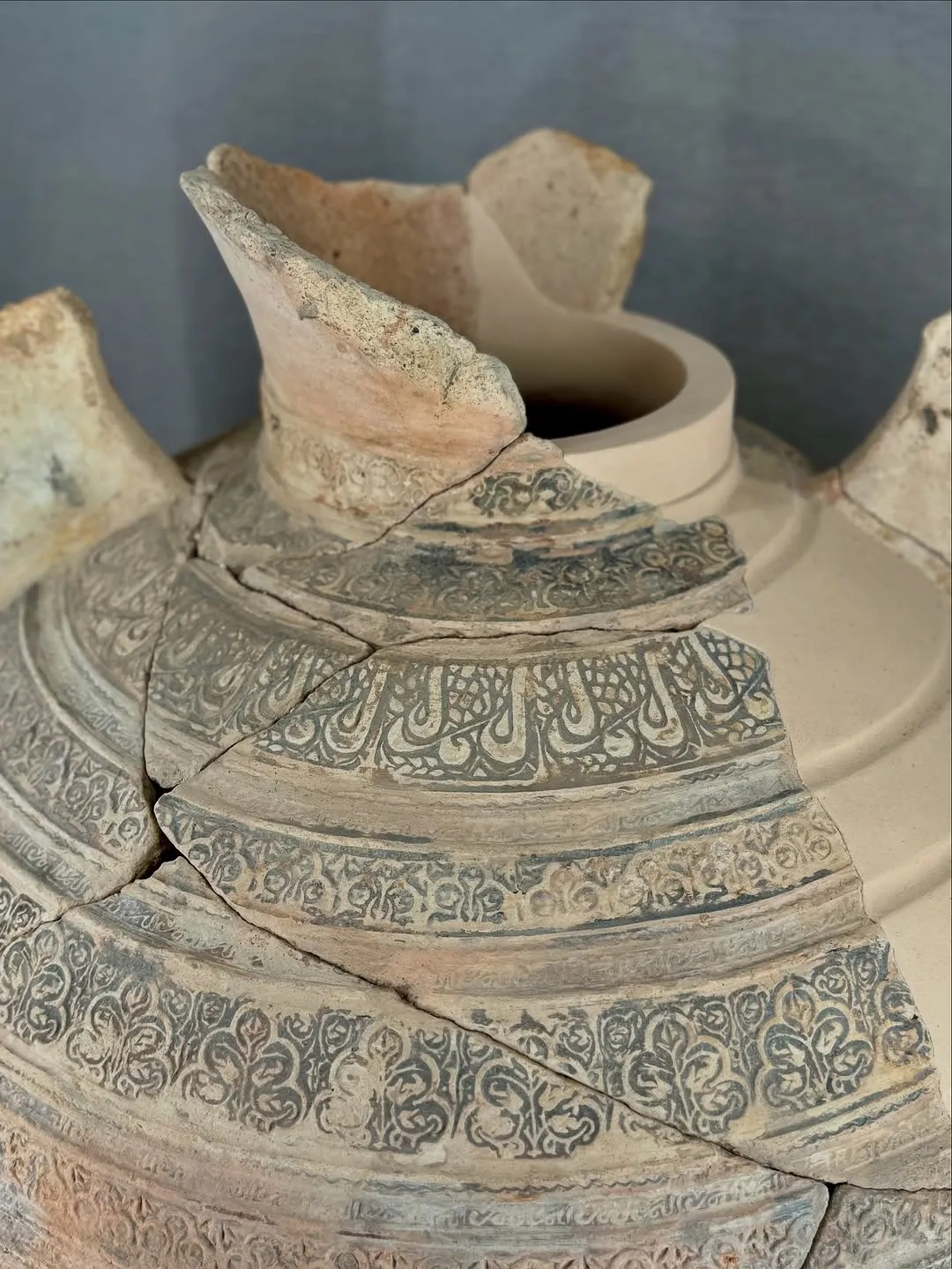 A close-up shot of an ancient, broken pottery vessel, showcasing intricate patterns. The image focuses on the detailed design and the texture of the aged ceramic.