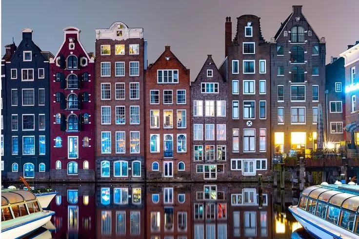 An iconic night view of traditional Dutch canal houses with illuminated windows perfectly reflecting in the still water below.