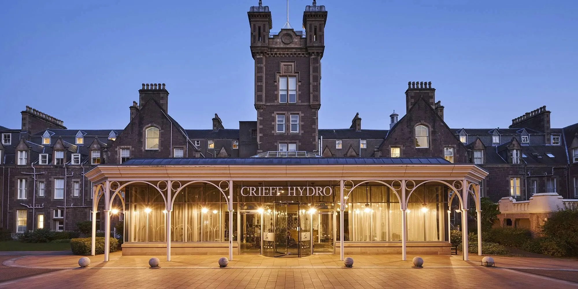 A high-quality image of the Crieff Hydro hotel exterior at dusk. The lighting is well-balanced, highlighting the architectural details, and the composition is symmetrical and visually appealing. The image is sharp, color-accurate, and photo-realistic, with all key elements in focus.