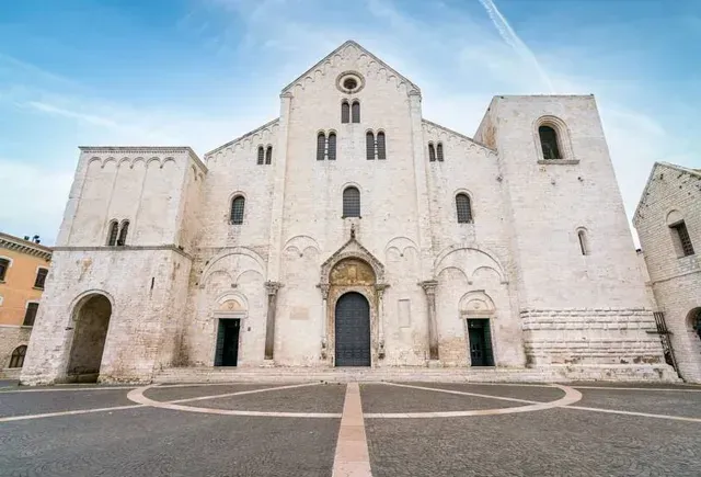 An imposing shot of a historic white stone cathedral facade under a clear blue sky, featuring intricate architectural details and a patterned plaza in the foreground.