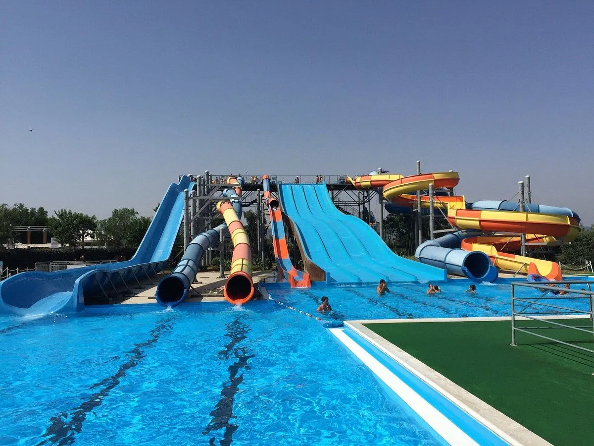 An image depicting a vibrant water park scene on a clear, sunny day, featuring multiple colorful water slides towering over a bright blue pool with people enjoying the water.