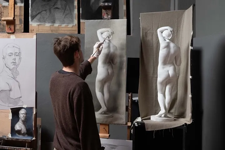 A photograph of an artist engaged in figure drawing within a studio setting, working from a classical sculpture.