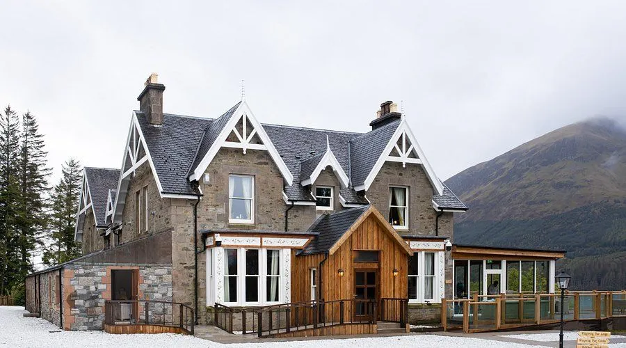 An appealing exterior shot of a stone and wood building, possibly a hotel or lodge, under an overcast sky. The image showcases architectural details and a welcoming entrance.