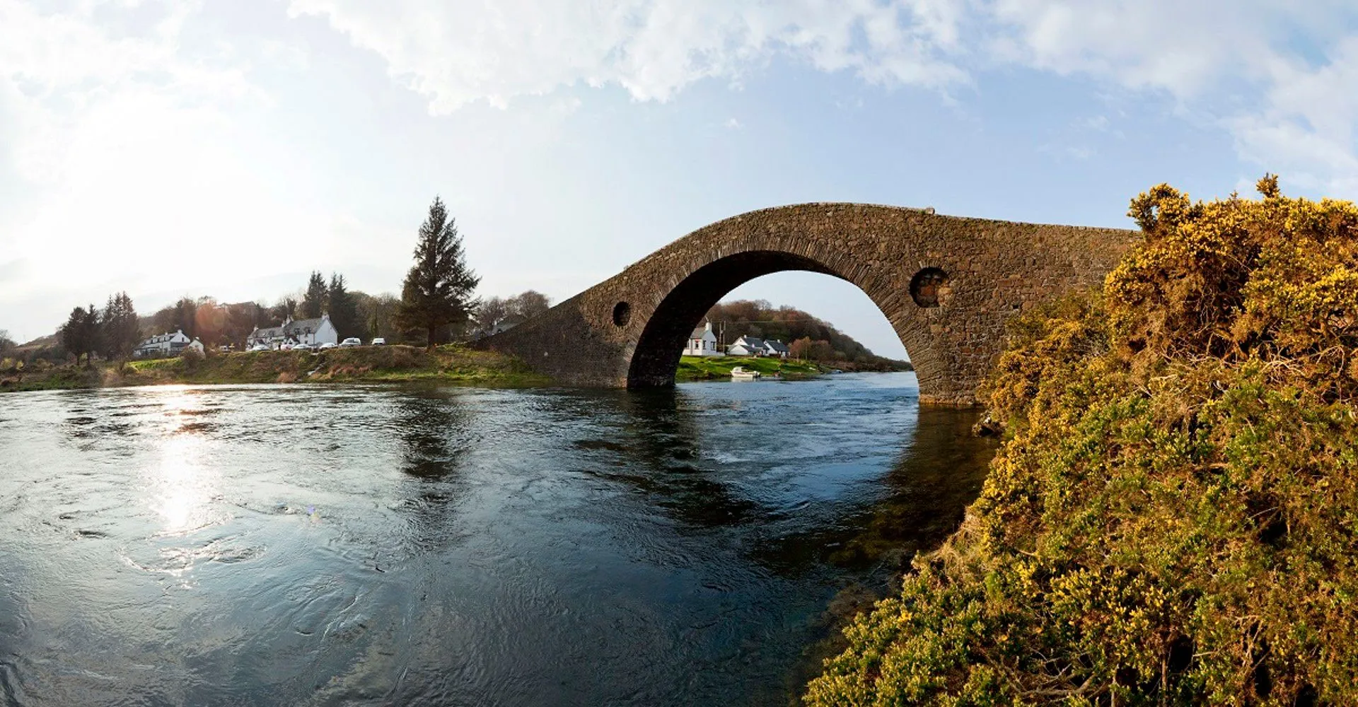 The image displays excellent photo-realism with strong sharpness on the stone bridge and water, capturing natural and vibrant colors under good lighting conditions. The composition effectively uses the bridge's arch to frame the scene.