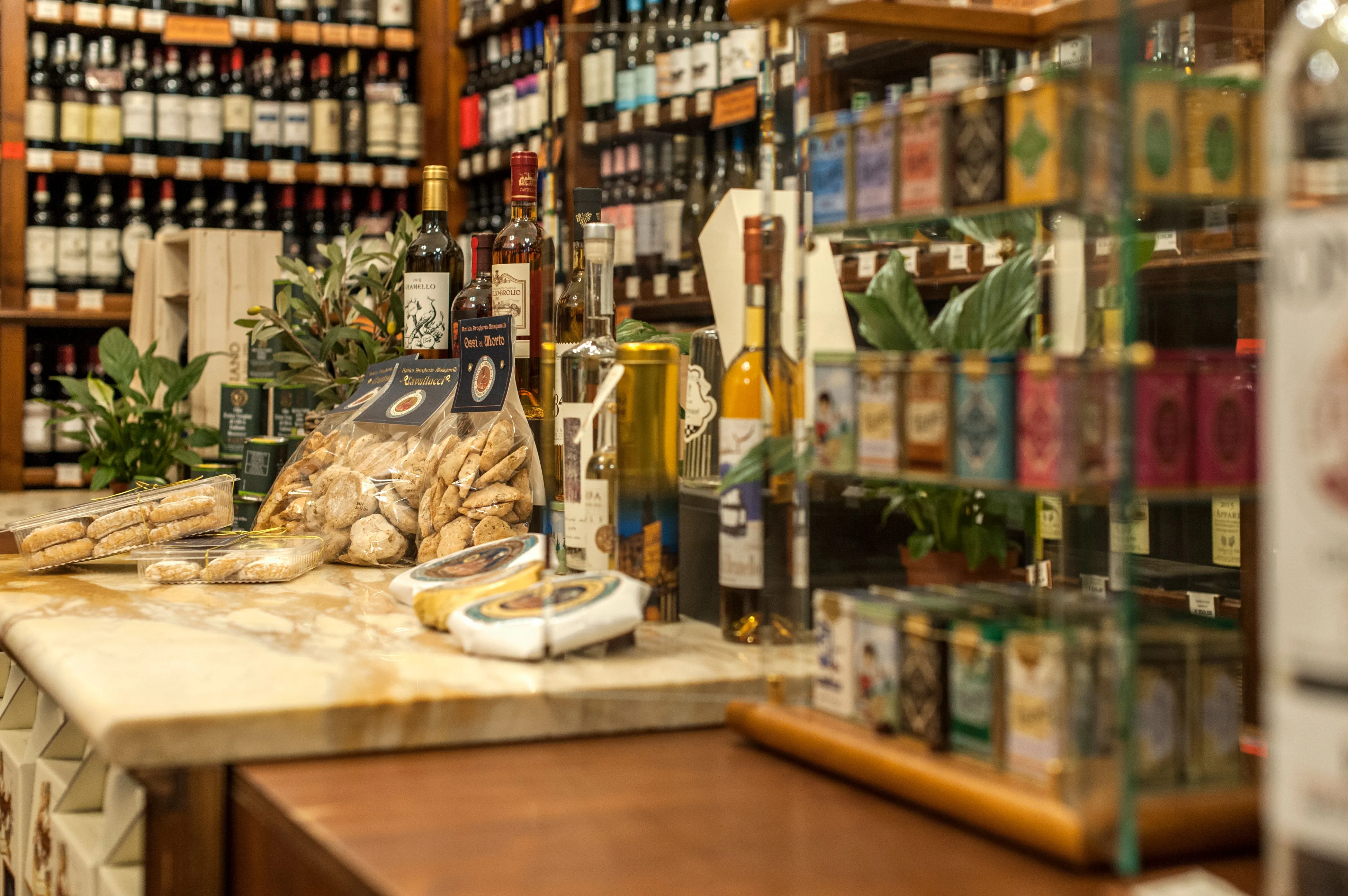 The image demonstrates strong composition with effective shallow depth of field, drawing attention to the foreground products. Key elements, such as the packaged goods and bottles, are sharp and accurately in focus. The lighting is natural and generally even, supporting the photo-realistic quality and accurate color representation. Overall, it's a high-quality editorial image of a shop interior.
