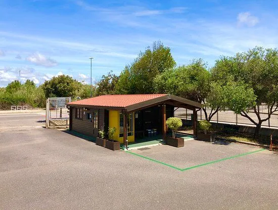The image features a small, rustic-style building with a red roof and a yellow door, surrounded by trees under a clear blue sky. The lighting is excellent, providing clear visibility of the structure and its surroundings. The image is sharp and appears photo-realistic with accurate colors. The main elements are well in focus.
