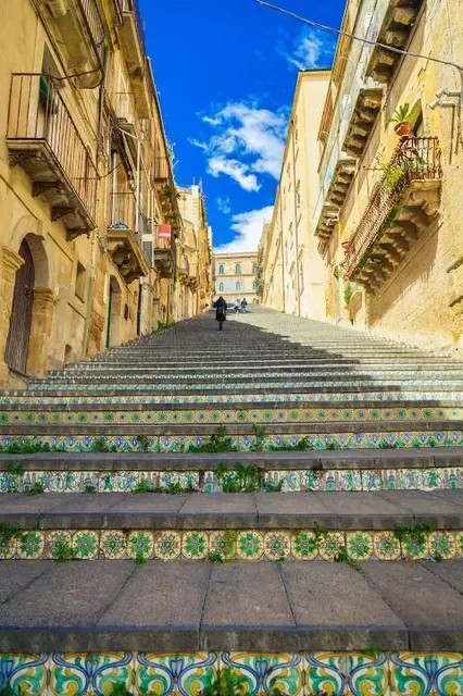 A well-composed and brightly lit image showcasing a long, ornate staircase ascending between historic buildings under a vibrant blue sky.