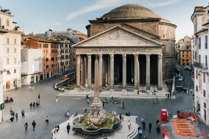 An elevated view of the Pantheon and Piazza della Rotonda in Rome, Italy, featuring the obelisk and fountain, with people populating the square.