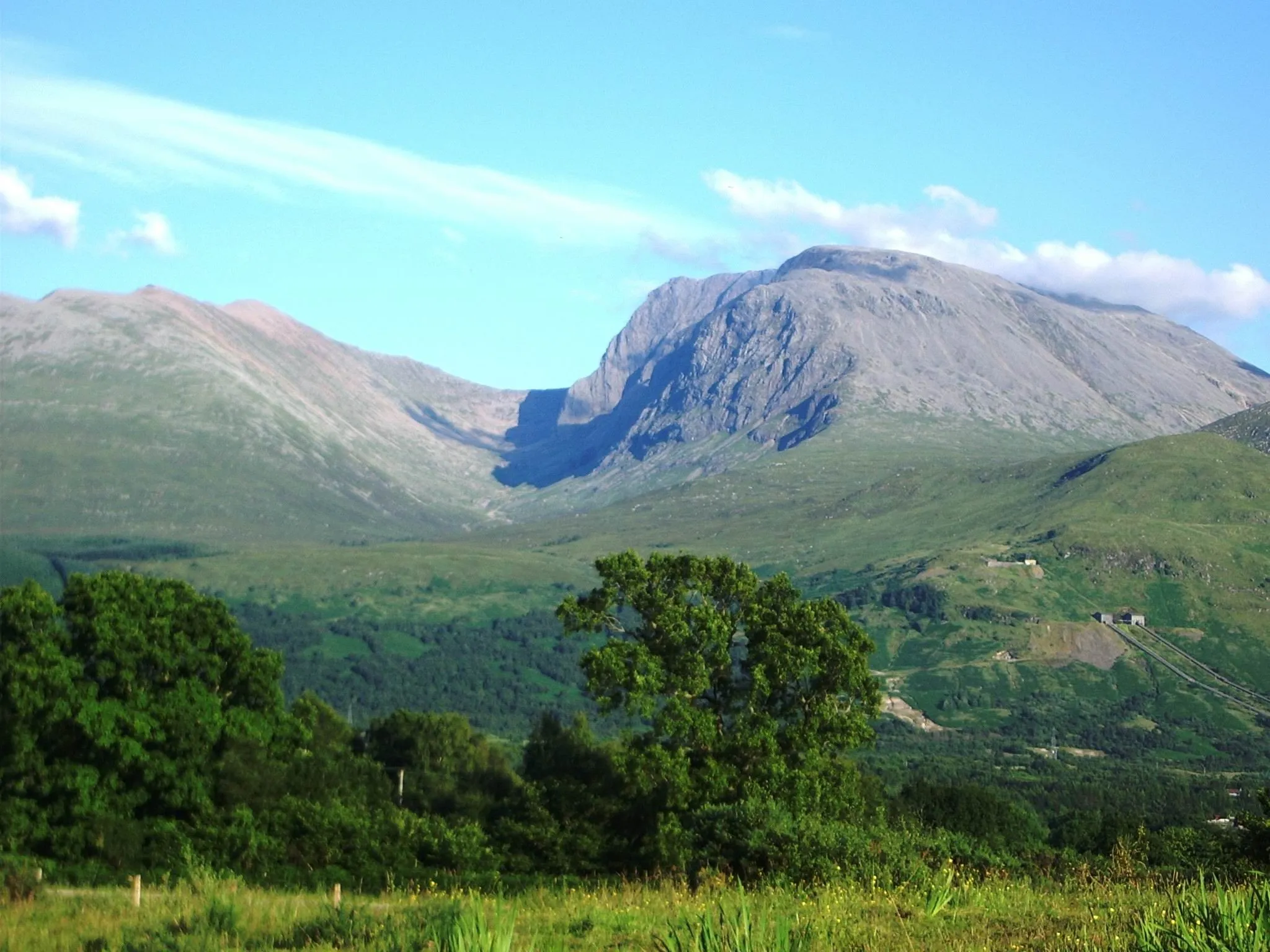 A scenic view of a mountain landscape with green valleys and trees under a clear blue sky.