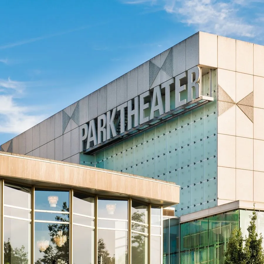 An architectural photograph of the 'PARKTHEATER' building exterior under a clear blue sky, featuring modern design elements like glass and concrete.