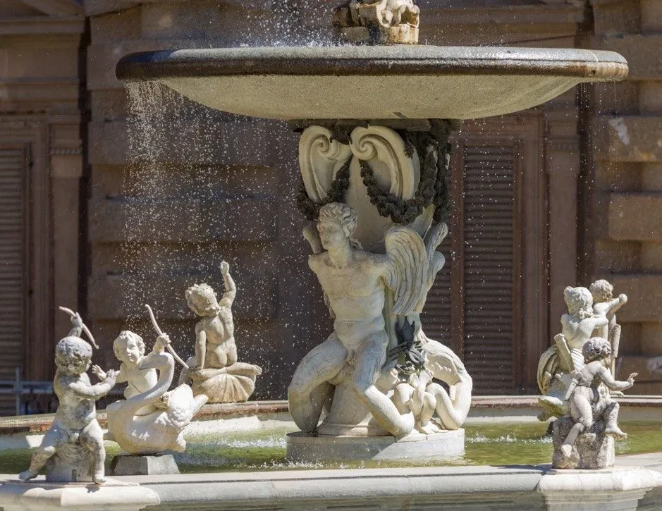 The image captures a detailed section of a classical fountain, featuring ornate stone sculptures and cascading water. The lighting is excellent, highlighting the intricate details of the statuary and the texture of the stone.