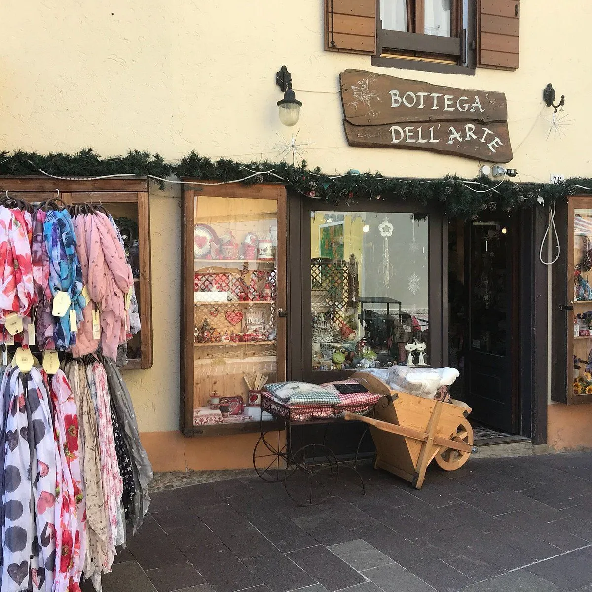 An image of a charming European storefront with scarves displayed outside and a sign reading "BOTTEGA DELL' ARTE".