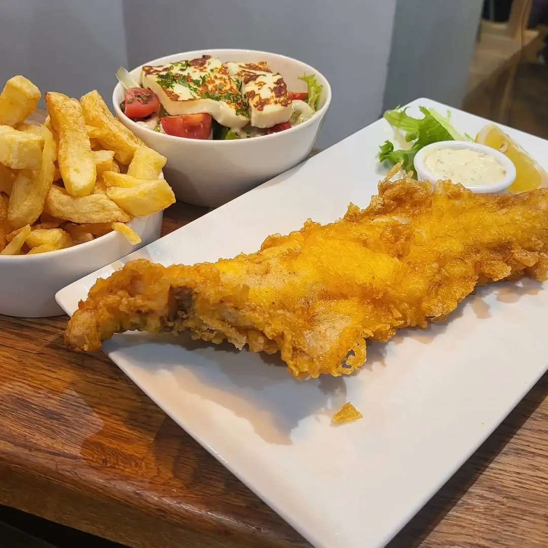 The image effectively showcases a classic fish and chips meal with a side salad. The composition is well-balanced, and the lighting effectively highlights the textures and colors of the food. The main elements, such as the fish and chips, are sharp and in focus, contributing to a highly photo-realistic and appetizing presentation.