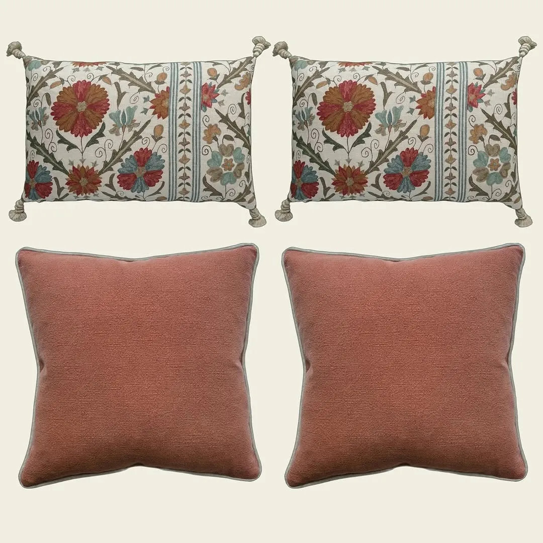 A professionally taken product image showcasing four pillows. The top two pillows feature a detailed floral pattern with tassels, while the bottom two are solid coral-colored. All are displayed against a neutral background.