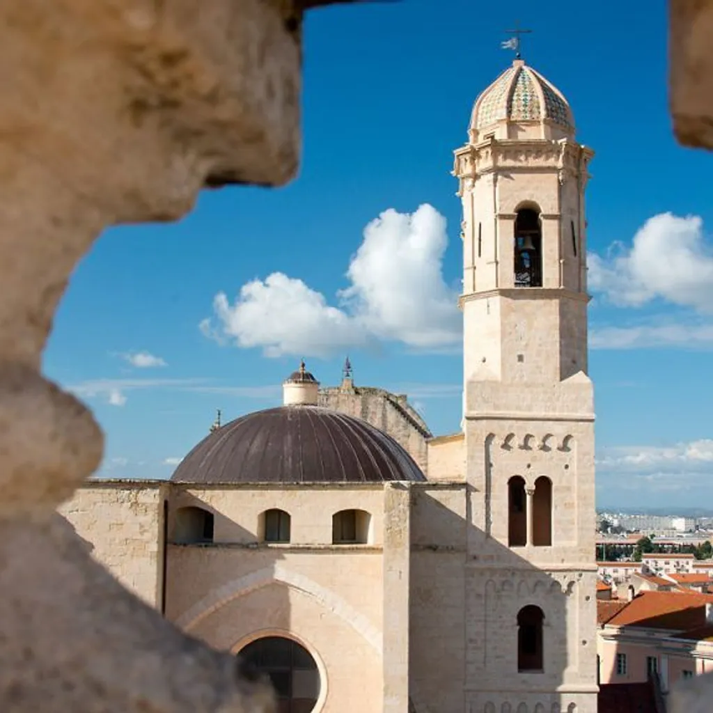 An editorial-style image showcasing a historic church or cathedral with a prominent bell tower and dome, framed by architectural elements in the foreground. The scene is set under a clear blue sky with white clouds, with a distant city skyline visible in the background.
