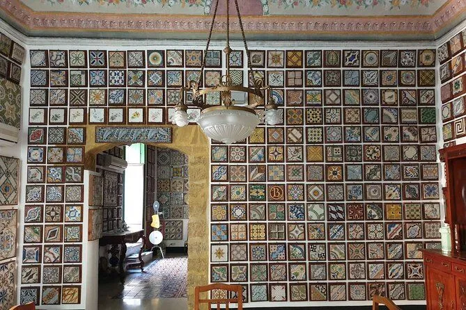 The image effectively captures a wall adorned with numerous decorative tiles and features a central chandelier. It exhibits good photo-realism, and the main elements, such as the tiles and the chandelier, are acceptably sharp and in focus. Colors appear accurate and natural to the scene. The primary weakness lies in the lighting, which is somewhat flat and lacks strong highlights or shadows, making the intricate tile work less dynamic than it could be. The composition is decent but could be improved for better visual flow and less prominence of the chandelier.