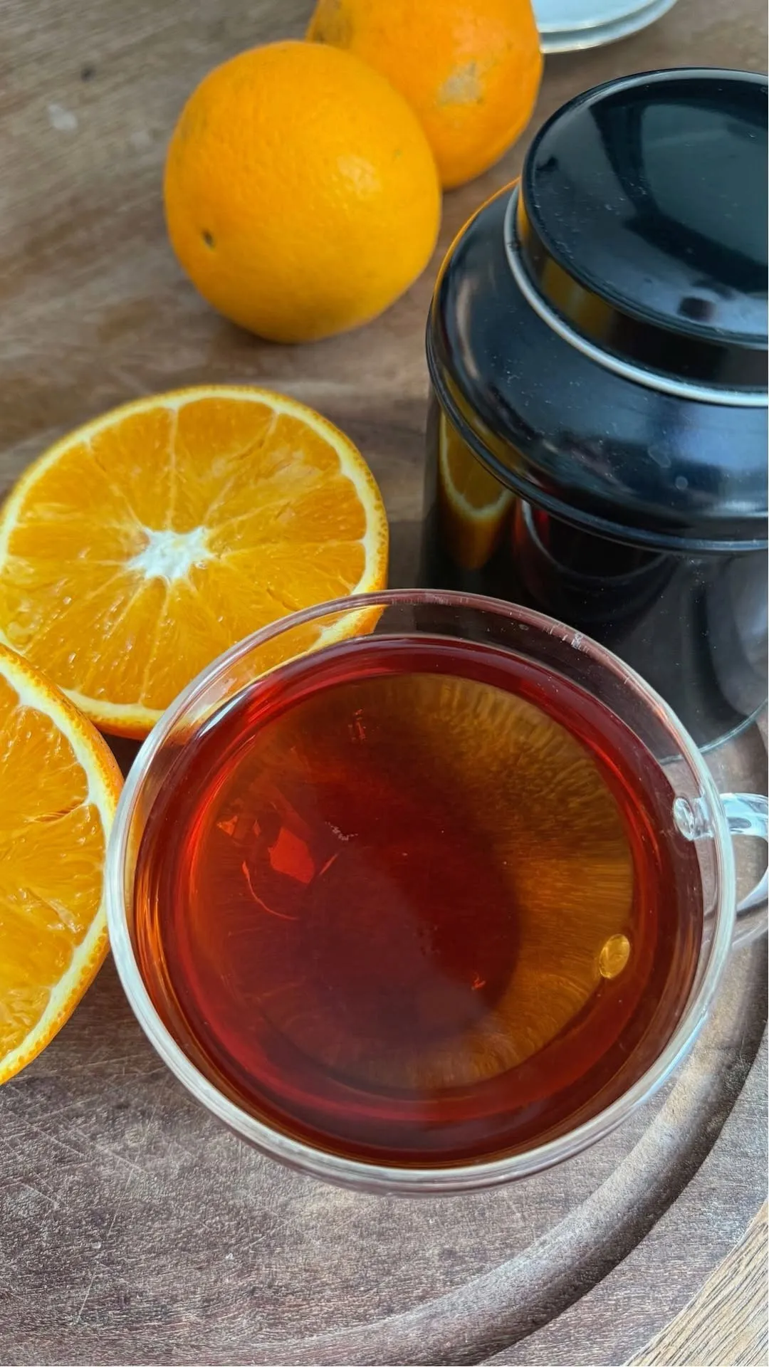 A well-composed close-up shot featuring a cup of tea, vibrant orange slices, and a black tin. The lighting is good, highlighting the rich colors and textures of the elements.