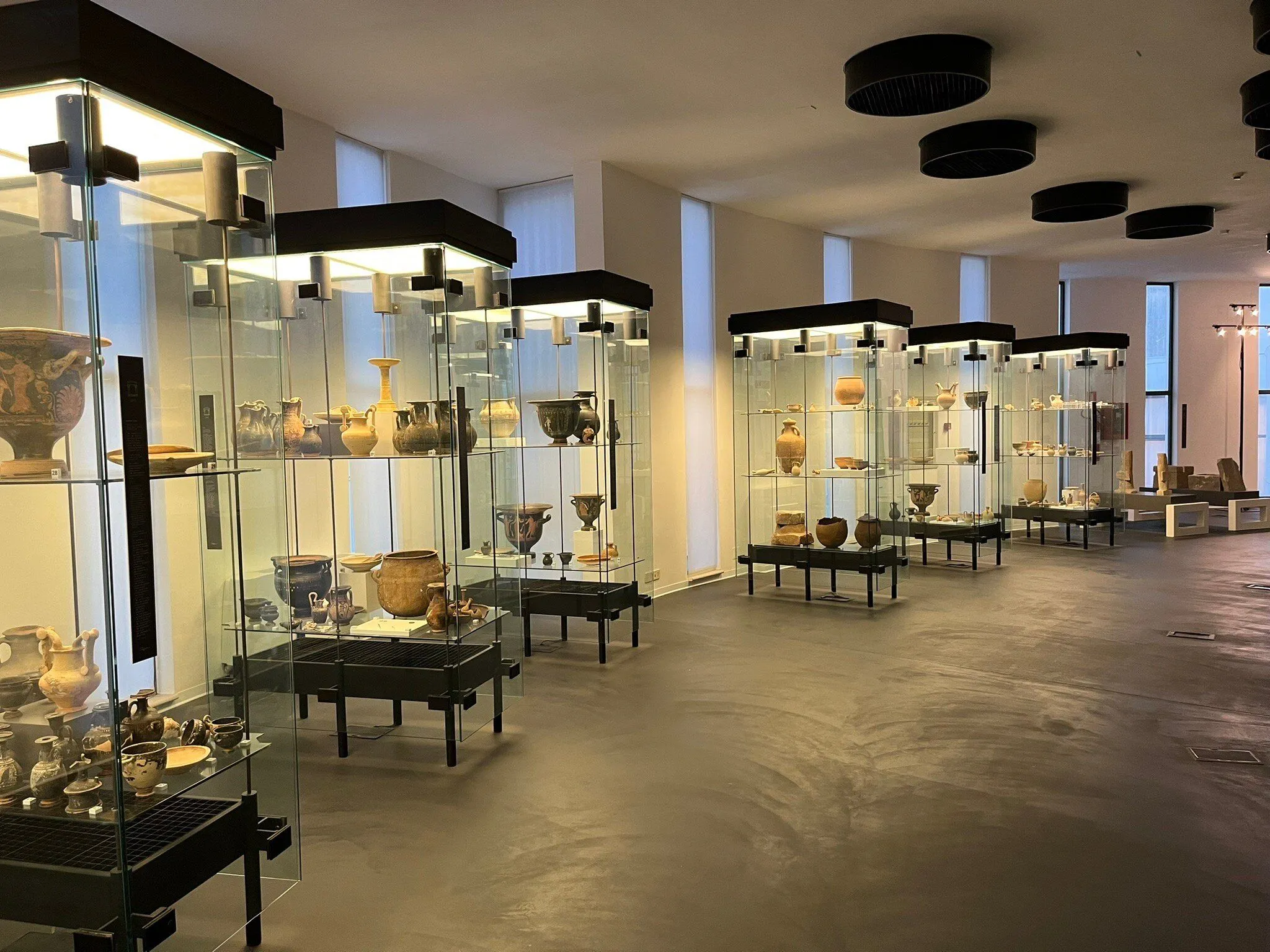 The image effectively captures a museum exhibition featuring ancient pottery in well-lit display cases. The artifacts are clearly visible and in focus, contributing to the photo-realistic quality. The colors appear accurate, reflecting the museum environment naturally.