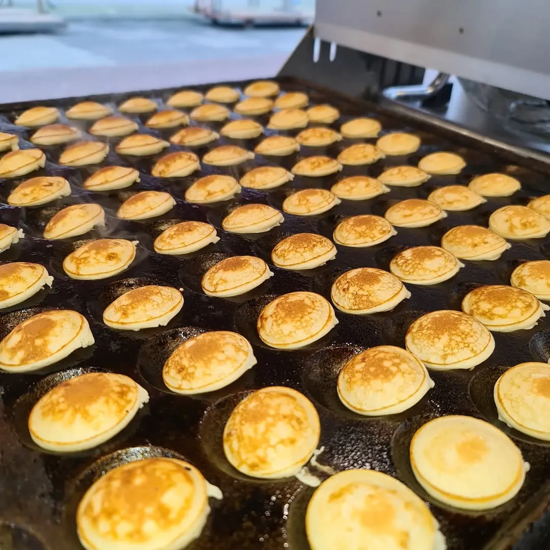 This image effectively captures the cooking process of mini pancakes (poffertjes) with good lighting and sharpness, especially on the main subjects. The colors are accurate, and the image is highly photo-realistic, making the food appear appealing. The composition is generally good, though a slightly different angle might enhance the visual impact further. There are no unwanted elements present.