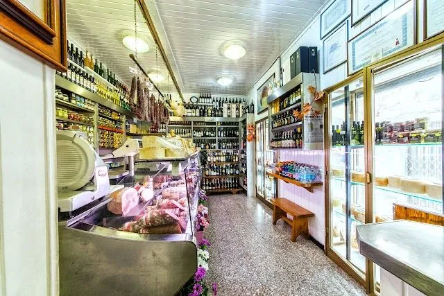 An interior view of a well-stocked traditional deli or grocery store, showcasing a variety of food items and beverages.