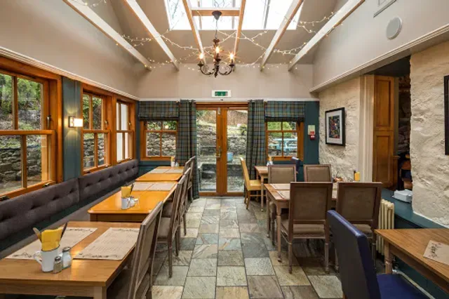 An empty dining room or restaurant interior with wooden tables and chairs, natural light from skylights and windows, and decorative lighting.