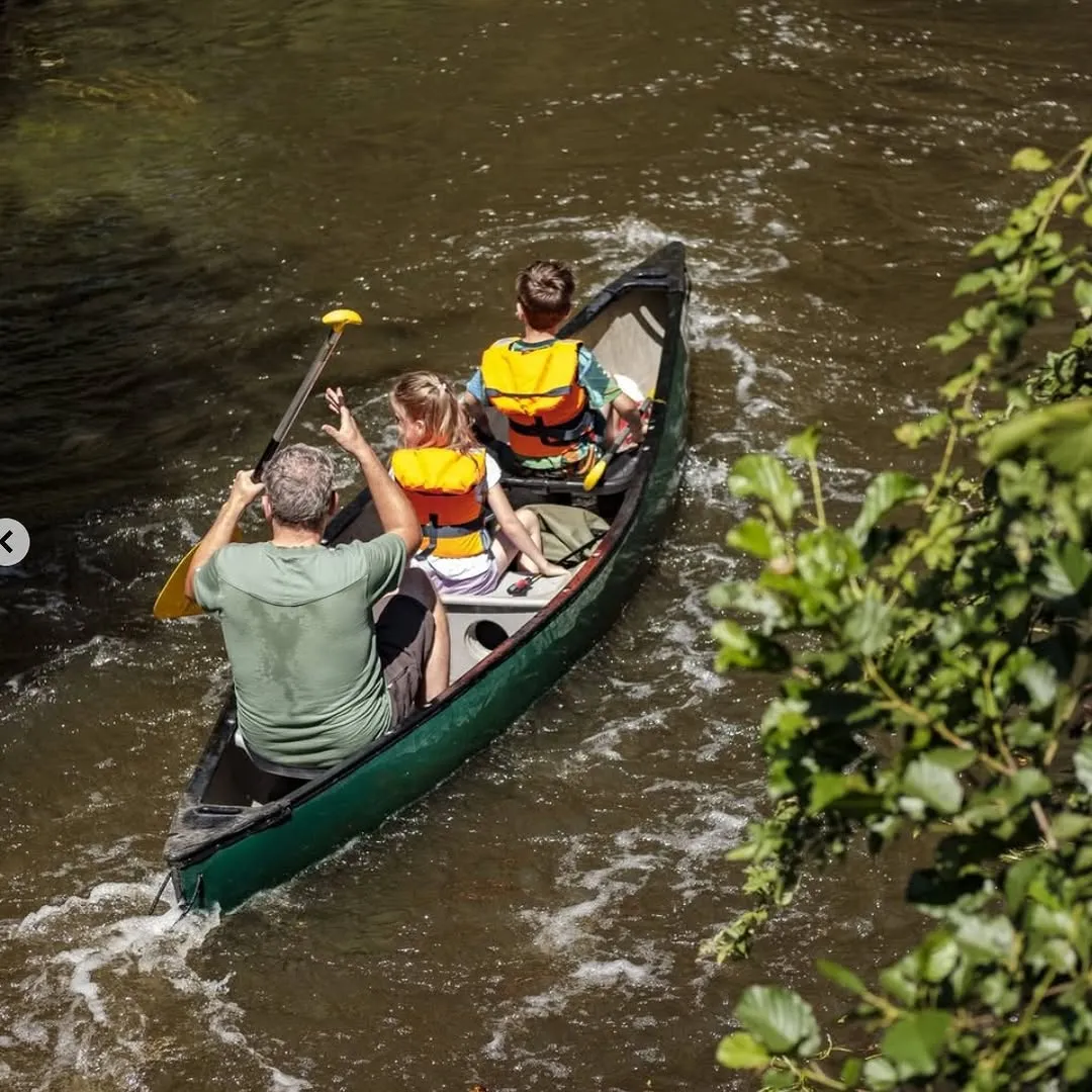 A high-quality, photo-realistic image depicting a family canoeing on a river. The composition is strong, showing the subjects and their activity clearly. The lighting is excellent, providing good visibility without harsh shadows, and the image is sharp with accurate, vibrant colors. Key elements are well in focus.