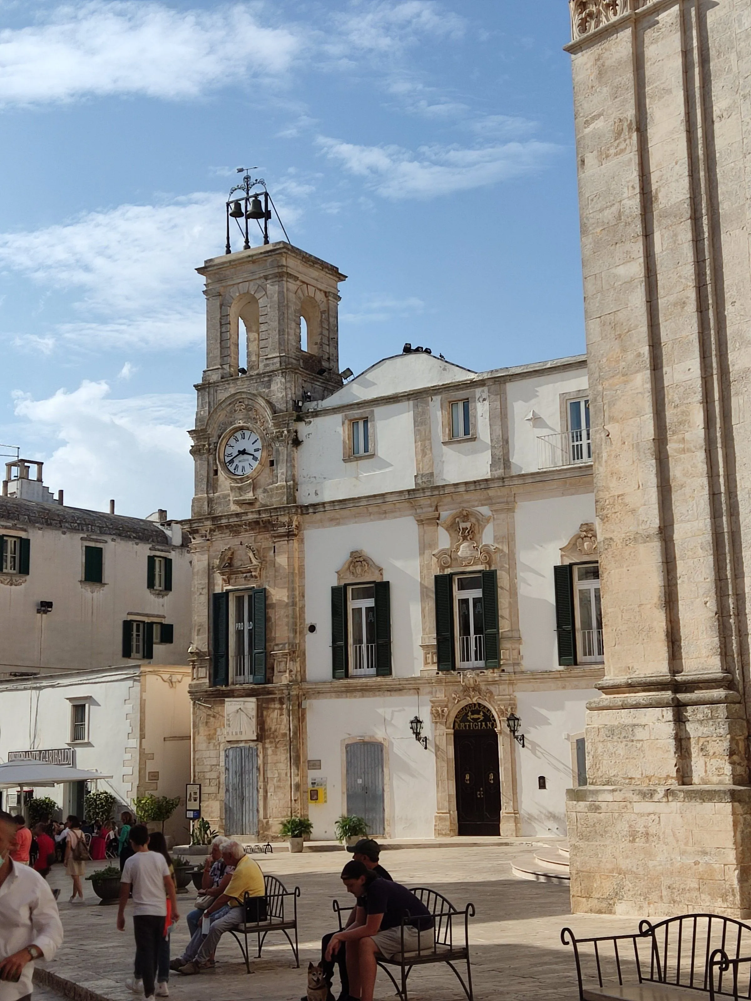 An editorial style image depicting a historic building with a prominent clock tower in a town square under clear daylight.