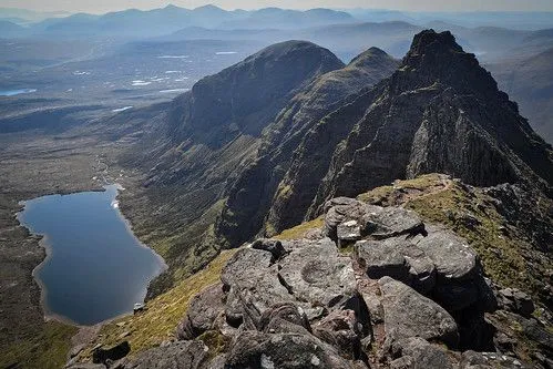 A well-composed and realistic landscape image featuring a vast mountainous terrain with a lake in the valley. The natural lighting highlights the textures of the rocks and mountains.