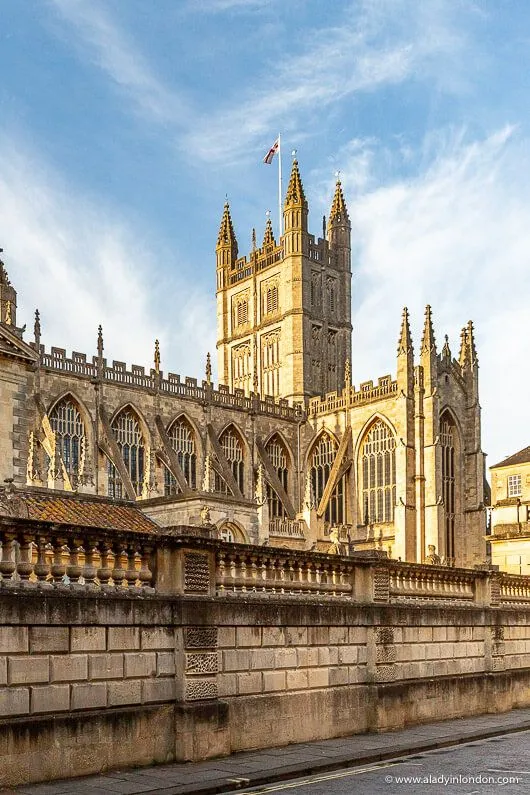 An editorial image featuring Bath Abbey, showcasing its detailed Gothic architecture and stone facade under a bright sky.