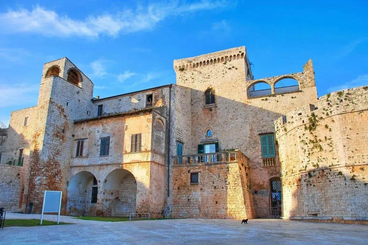 An impressive view of a historical stone building or castle under a clear blue sky, featuring intricate architectural details and a spacious courtyard.