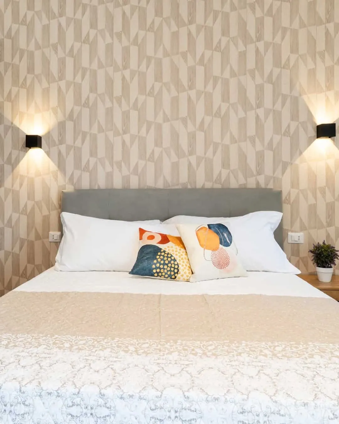 The image showcases a well-lit and sharp bedroom interior, highlighting the bed with its decorative pillows, headboard, and geometric wallpaper. The colors are accurate, and all key elements are in sharp focus, contributing to a high degree of photo-realism. The composition is clean and centered, presenting the space effectively.