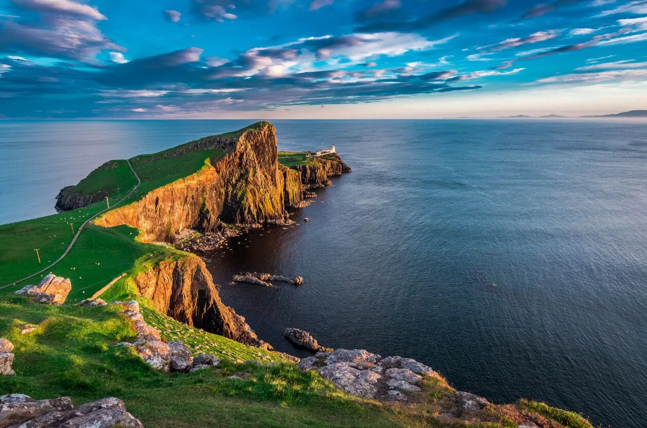 An exceptionally high-quality image of a lighthouse atop a dramatic cliff face overlooking the ocean under a beautiful sky.